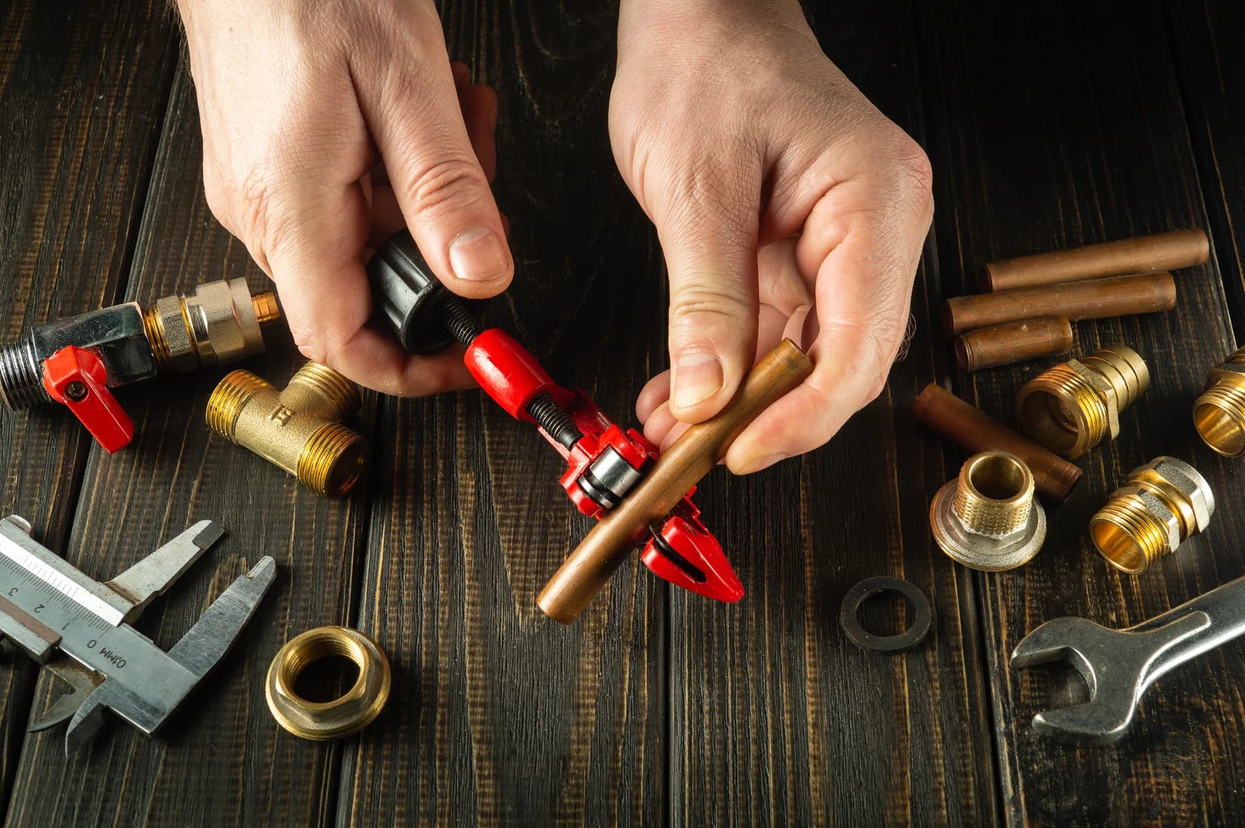 Hände eines Handwerkers kürzen ein Kupferrohr mit einem Rohrschneider