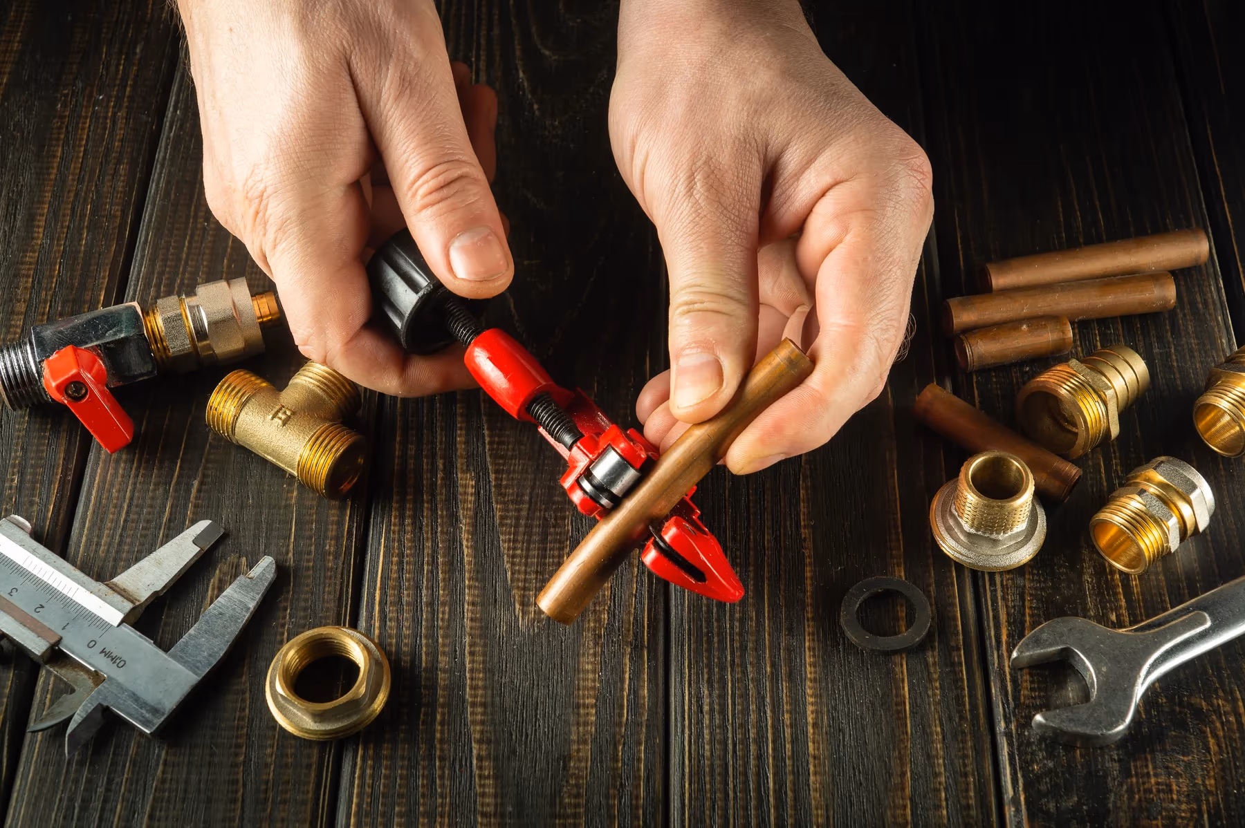 Hände eines Handwerkers kürzen ein Kupferrohr mit einem Rohrschneider